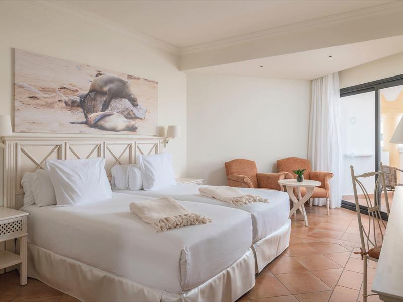 Lichte hotelkamer met groot bed, zithoek en balkon met uitzicht op zee.