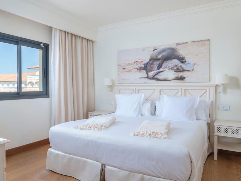 Licht ingerichte hotelkamer met twee eenpersoonsbedden, zeezicht en dolfijnenfoto boven de bedden.