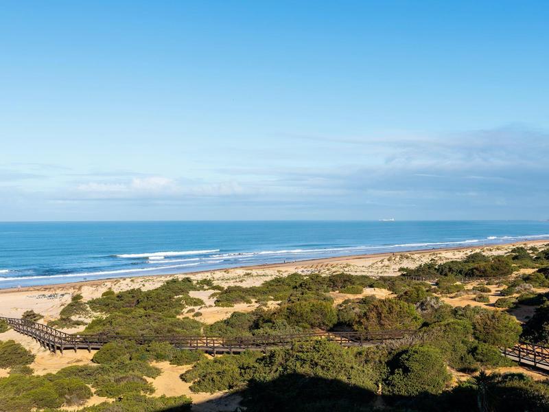 Uitgestrekt zandstrand met duinen en heldere blauwe lucht bij de zee.