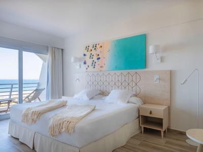 Helles Schlafzimmer mit Doppelbett, weißen Wänden, buntem Wandbild und Meerblick durch große Fenster.