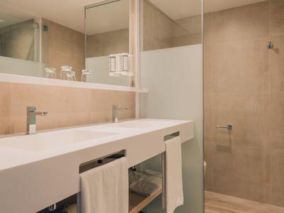 Helles Badezimmer mit Doppelwaschbecken, großen Spiegeln und beigem Fliesen-Duschenbereich.