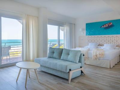 Lichte hotelkamer met tweepersoonsbed, blauwe bank, zeezicht en balkon.