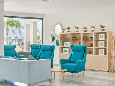 Helles Wohnzimmer mit blauen Sesseln, grauem Sofa, Holzregal und großem Fenster zum Garten.