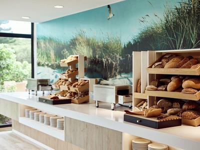 Moderne Bäckerei mit weißem Tresen, Holzregalen voller frischer Brote und großer Naturwandgestaltung.