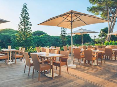 Terras met houten vloer, tafels, stoelen en grote parasols in een groene omgeving.