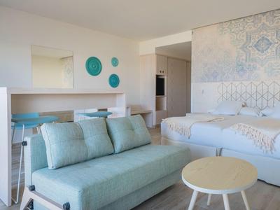 Helles Hotelzimmer mit zwei Betten, blauem Sofa, Tisch und dekorativen Wandakzenten.