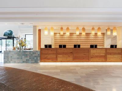 Moderne Hotelrezeption mit hölzernen Tresen, warmem Licht und hellem Marmorfußboden.