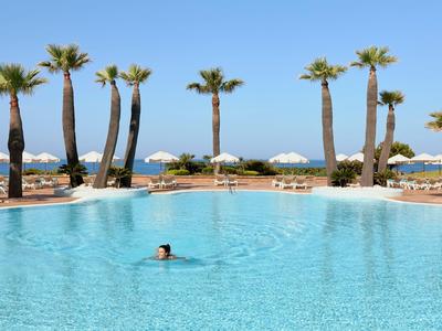 Großer Pool mit klarem blauen Wasser, Palmen am Rand und Person schwimmt darin.