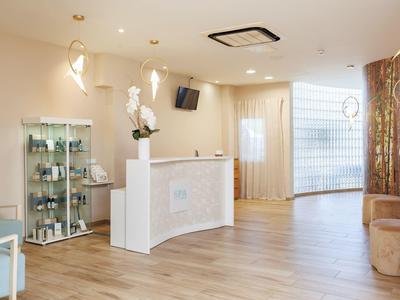 Heller Empfangsbereich mit weißem Tresen, Vitrine, Holzfußboden und schlichten Sitzmöglichkeiten.