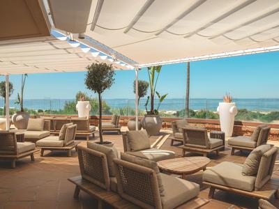 Buitenlounge met zitgroepen en uitzicht op zee onder een lichte zonwering