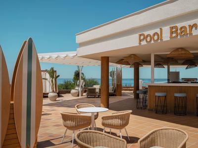 Buitenpoolbar met stoelen, tafels en surfplanken op een zonnig strand.