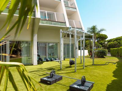 Moderner Hotelgarten mit Fitnessgeräten auf grünem Rasen und Balkon im Hintergrund.