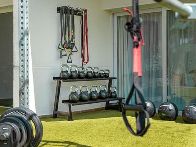 Fitnessgeräte und -gewichte auf grünem Kunstrasen vor einem Hotelzimmer mit Glasschiebetür.