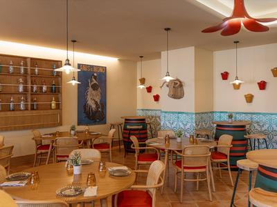 Modernes Hotelrestaurant mit Holztischen, bunten Stühlen und dekorativen Lampen an der Decke.
