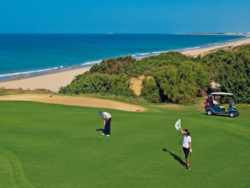 Golfspelers op een groen veld met oceaan en strand op de achtergrond.