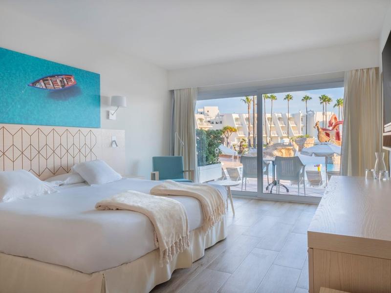 Modern hotelkamer met twee bedden en uitzicht op een terras met palmbomen.