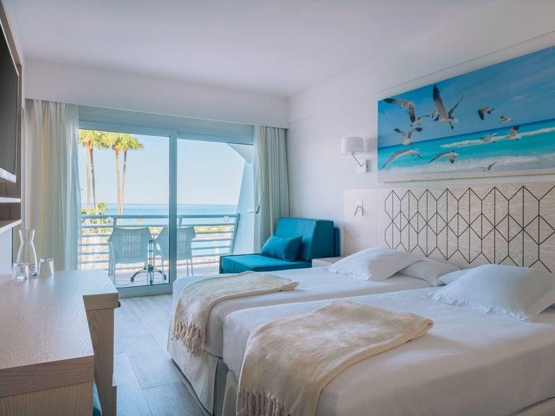 Modern hotelkamer met twee bedden, zeezicht en balkon met zitgedeelte.