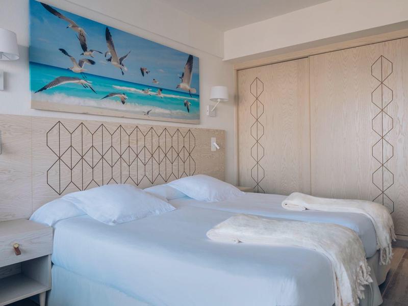 Hotelkamer met twee eenpersoonsbedden, witte handdoeken en zee-thema wanddecoratie.