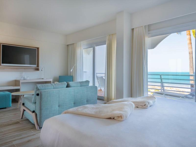 Lichte hotelkamer met balkon, zeezicht, tv en moderne inrichting.