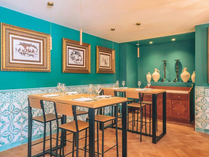 Elegante eetruimte met hoge tafels, stoelen en turquoise muren met kunstwerken.