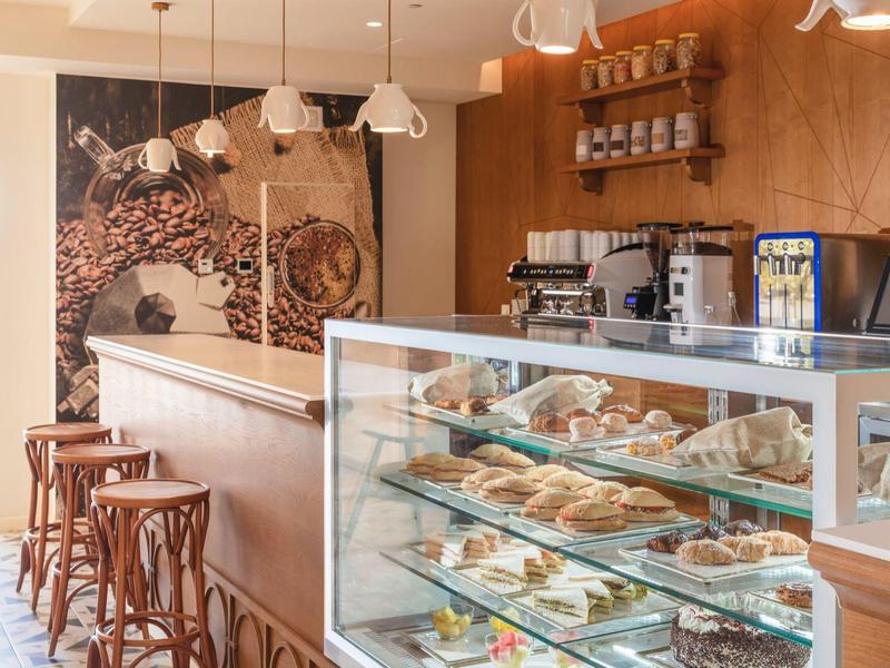 Moderne bakkerij met houten toonbank, krukken en glazen vitrine vol gebak.