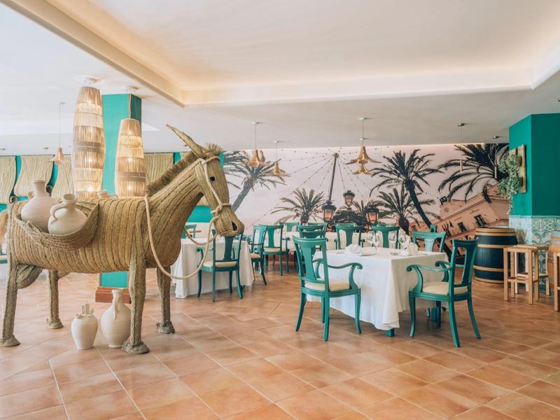 Hotelrestaurant met maritieme muurschildering, decoratief paardenbeeld en blauw-witte stoelen.