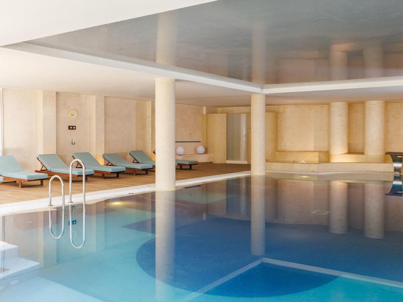 Overdekt zwembad met helder water, ligstoelen en lichte houten bekleding.
