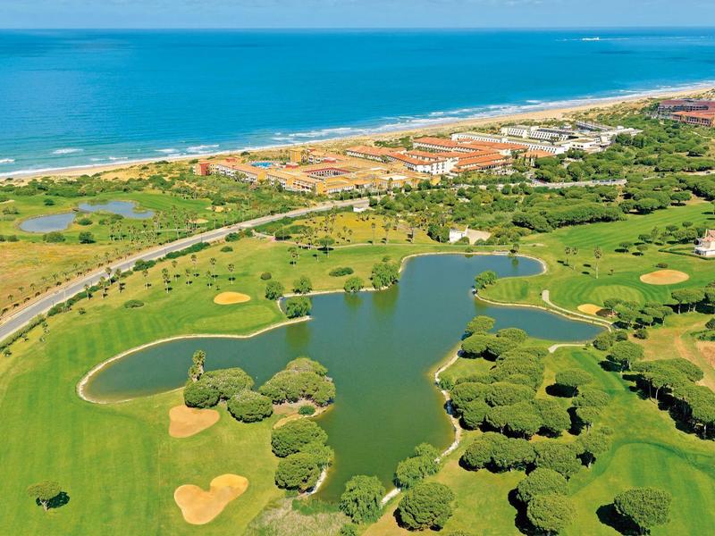 Luchtfoto van een golfbaan met waterhindernissen en een strand op de achtergrond.