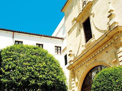 Cour intérieur lumineux avec arbres ronds et bâtiment historique sous un ciel bleu clair.