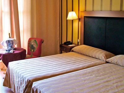 Chambre d'hôtel avec deux lits simples, lampe de chevet, chaise et rideaux.