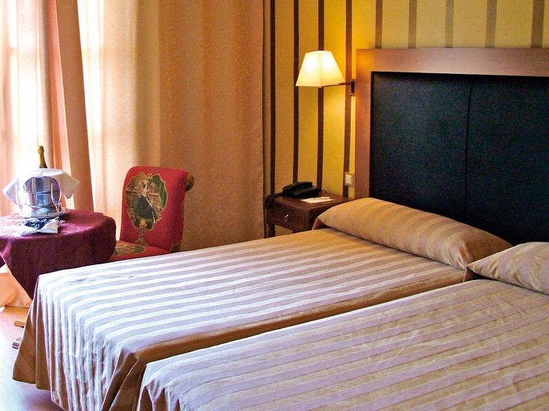 Chambre d'hôtel avec deux lits simples, lampe de chevet, chaise et rideaux.