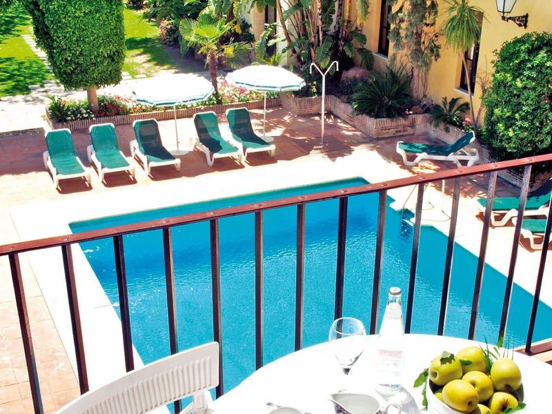 Vue d'une piscine avec des chaises longues, des parasols et une table avec un petit déjeuner au premier plan.