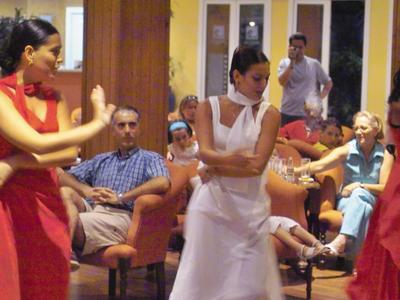 Trzy kobiety tańczą w kolorowych sukienkach przed publicznością w pomieszczeniu.