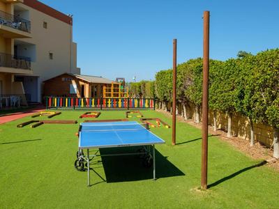 Ein Tischtennistisch auf grünem Kunstrasen neben einem Wohngebäude und Spielplatz.