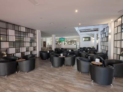 Moderner, heller Lounge-Bereich mit schwarzen Ledersesseln und Holzfußboden, geräumig und einladend.