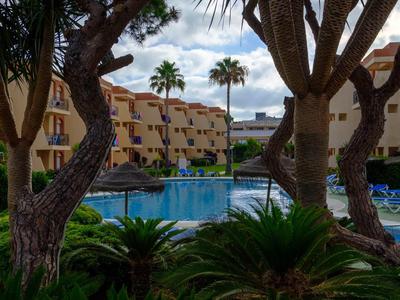 Widok na hotelowy basen otoczony palmami i wielopiętrowymi budynkami.