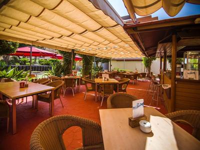 Überdachte Terrasse eines Cafés mit Holztischen, Stühlen und warmem Sonnenlicht.
