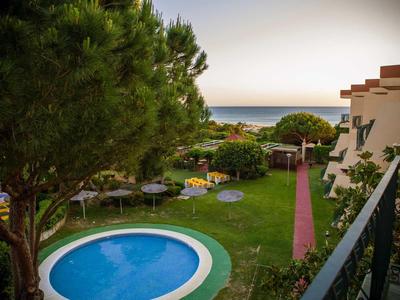 Runder Pool im Garten mit grünen Bäumen und Blick aufs Meer im Hintergrund bei Sonnenuntergang.