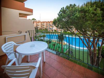 Balkon mit weißem Tisch, zwei Stühlen und Blick auf Pool und gepflegten Garten.