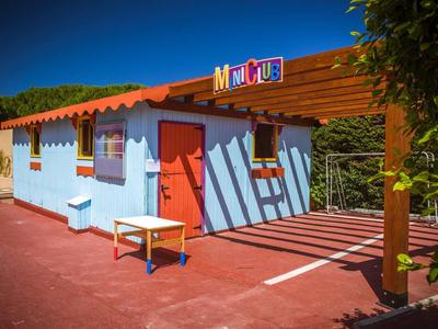 Buntes Kinderhaus mit blauen Wänden, rotem Dach und Schattenmuster auf rotem Asphalt.