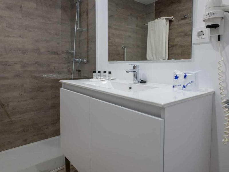 Weißes Badezimmerschrank mit Waschbecken, großem Spiegel und Dusche mit Holzoptikfliesen.