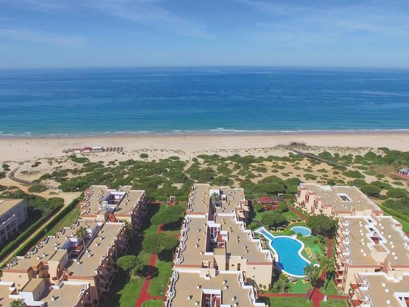 Große Wohnanlage mit mehreren Gebäuden und Pools an einem langen Sandstrand mit blauem Meer.