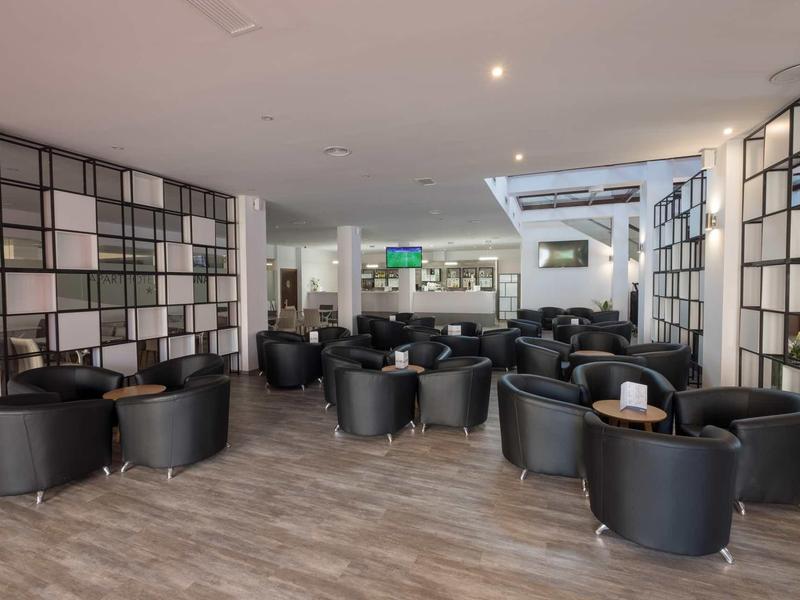 Moderner, heller Lounge-Bereich mit schwarzen Ledersesseln und Holzfußboden, geräumig und einladend.