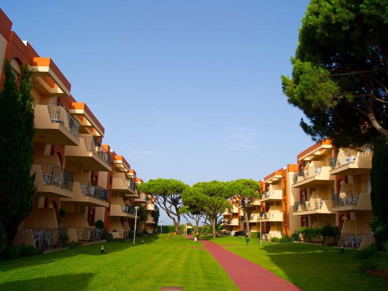 Grüne Rasenfläche mit rotem Weg zwischen mehrstöckigen hellen Wohngebäuden unter blauem Himmel.