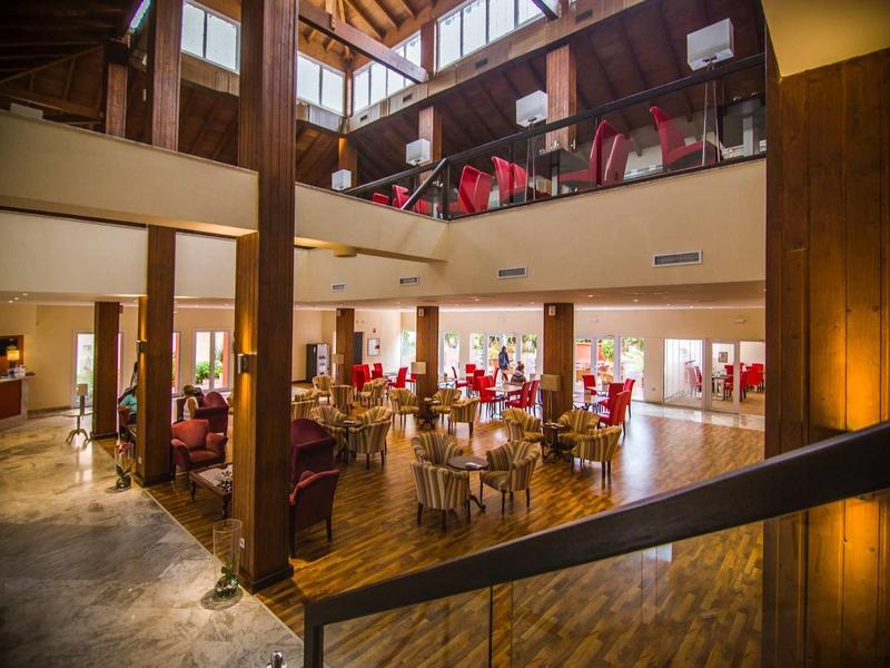 Großer, heller Gastraum mit Holzsäulen, roten Stühlen und bodentiefen Fenstern in gemütlichem Stil.