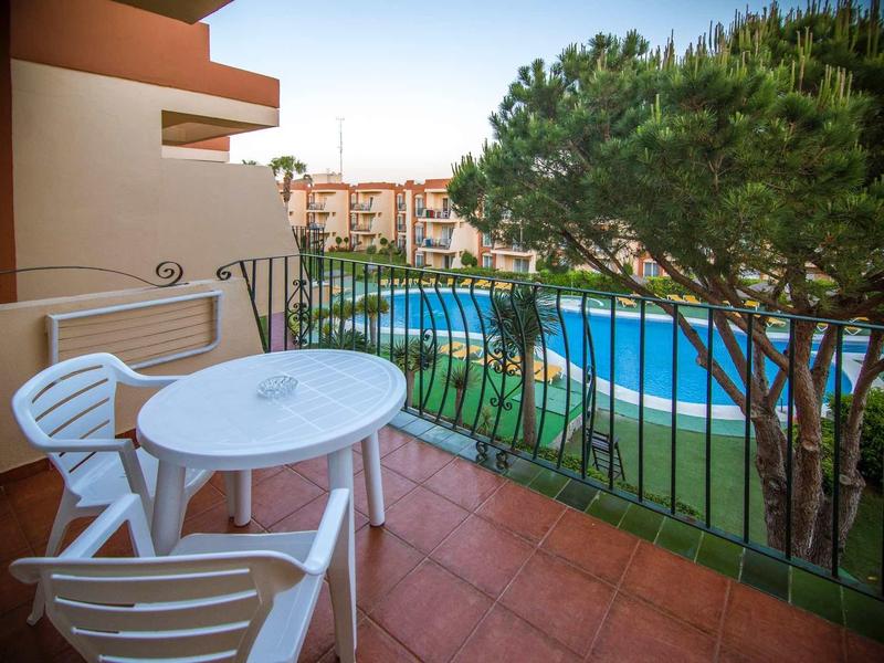 Balkon mit weißem Tisch, zwei Stühlen und Blick auf Pool und gepflegten Garten.