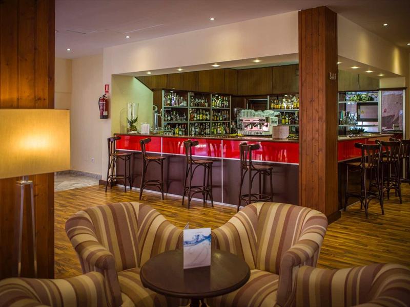 Moderne Bar mit roten Barhockern, hölzernen Möbeln und bequemen gestreiften Sesseln im Vordergrund.