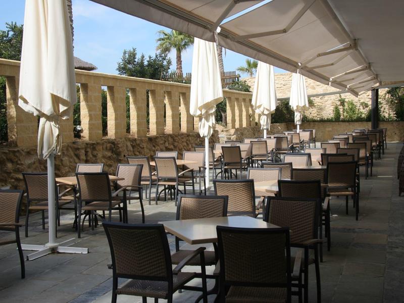 Area esterna vuota di un bar o ristorante con tavoli e sedie sotto una copertura.