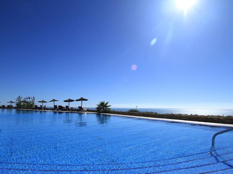 Grande piscina all'aperto con acqua limpida e ombrelloni sotto un cielo azzurro.