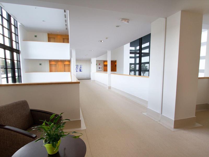 Corridoio d'hotel luminoso con grandi finestre, area salotto e ingressi delle camere.